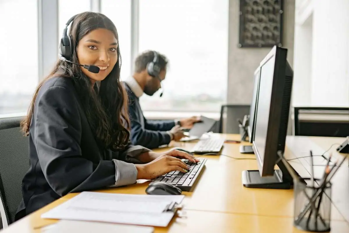 A woman wearing a headset and working on a computer in an office environment.
