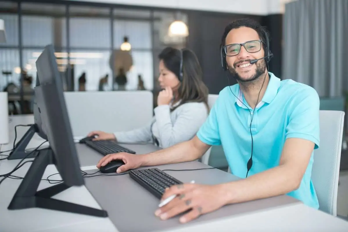 Two customer service representatives working at desks with computers and headsets in an office environment.
